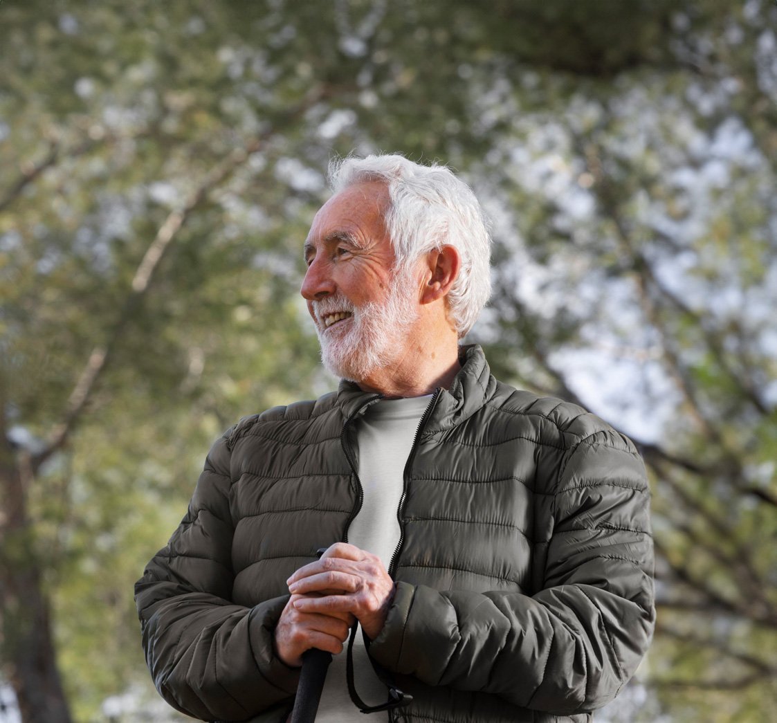 Hombre mayor sonriente disfrutando del aire libre mientras lleva audífonos discretos que mejoran su capacidad auditiva, brindados por Aurical, centro auditivo especializado en soluciones para la hipoacusia.